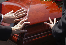 A group of people holding their hands out to a wooden coffin.